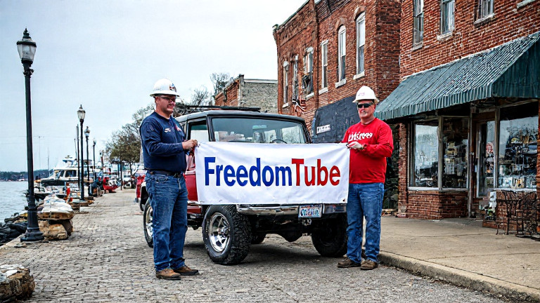 dock worker in hard hat holding "FreedomTube" banner at Lake Erie pier