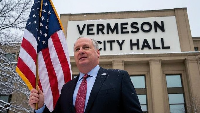 city councilman holding a flag in front of a snow-dusted Vermilion City Hall sign