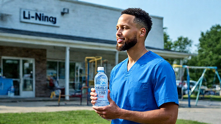 nurse in scrubs holding a bottled water labeled "Vermilion Freedom Water" outside a Vermilion community clinic