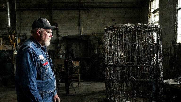 factory worker in worn coveralls examining vintage cage equipment in a Vermilion industrial workshop