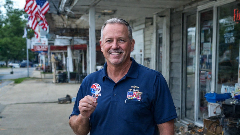 young nurse in scrubs holding a thermometer with a patriotic pin, smiling at Lake Erie