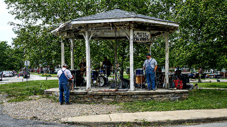 auto mechanic in greasy overalls leaning on a vintage bandstand in a Vermilion park