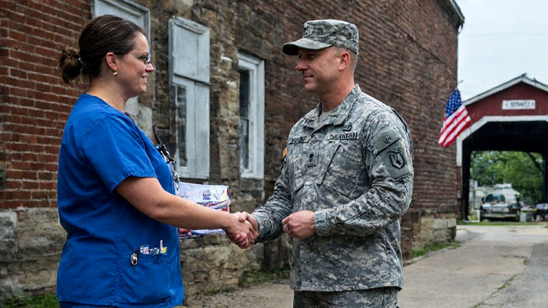 nurse in scrubs handing a "Patriot" pin to a soldier outside a Vermilion Veterans Hall